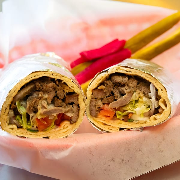 Two halves of a Shawarma Mediterranean Grill shawarma wrap, filled with meat, lettuce, and tomatoes, with pickles.