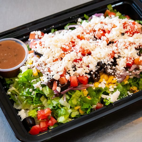 A Mediterranean salad with lettuce, tomatoes, olives, corn, red onion, and feta cheese.