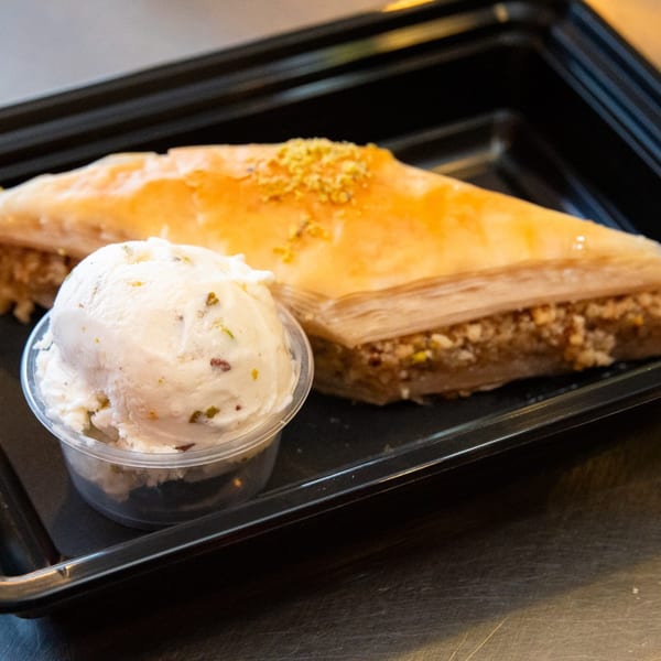 A triangular piece of baklava with pistachio topping next to a scoop of ice cream.