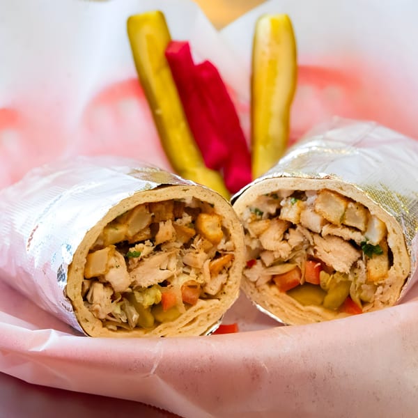 Two shawarma wraps, cut in half, filled with chicken and vegetables, served with pickles.