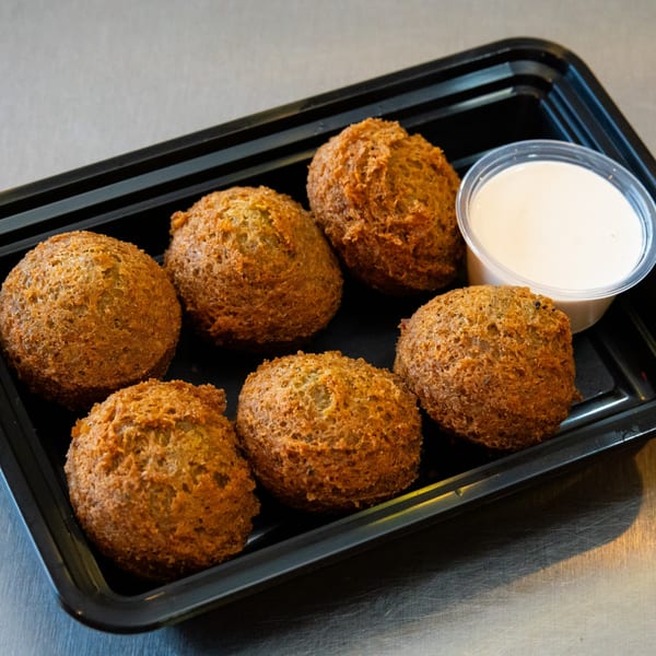 Six golden-brown falafel balls and a small cup of white sauce in a black to-go container.