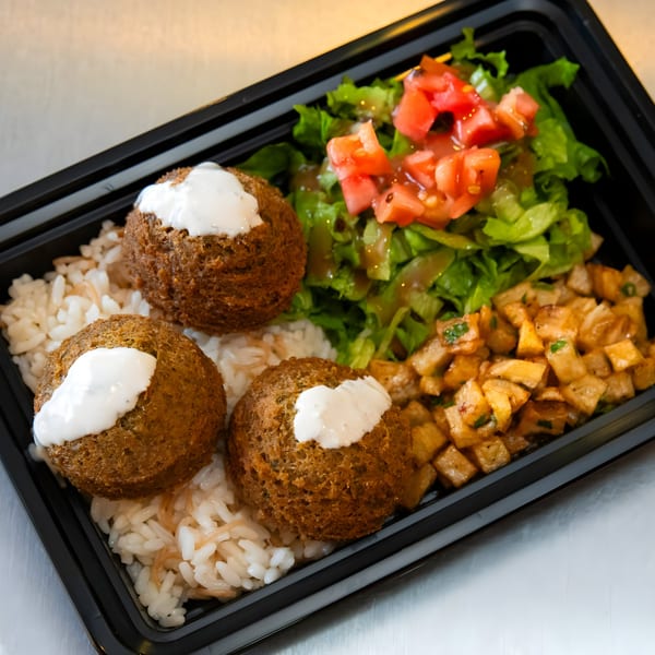 Shawarma Mediterranean Grill falafel plate with rice, salad, and seasoned potatoes in a black container.